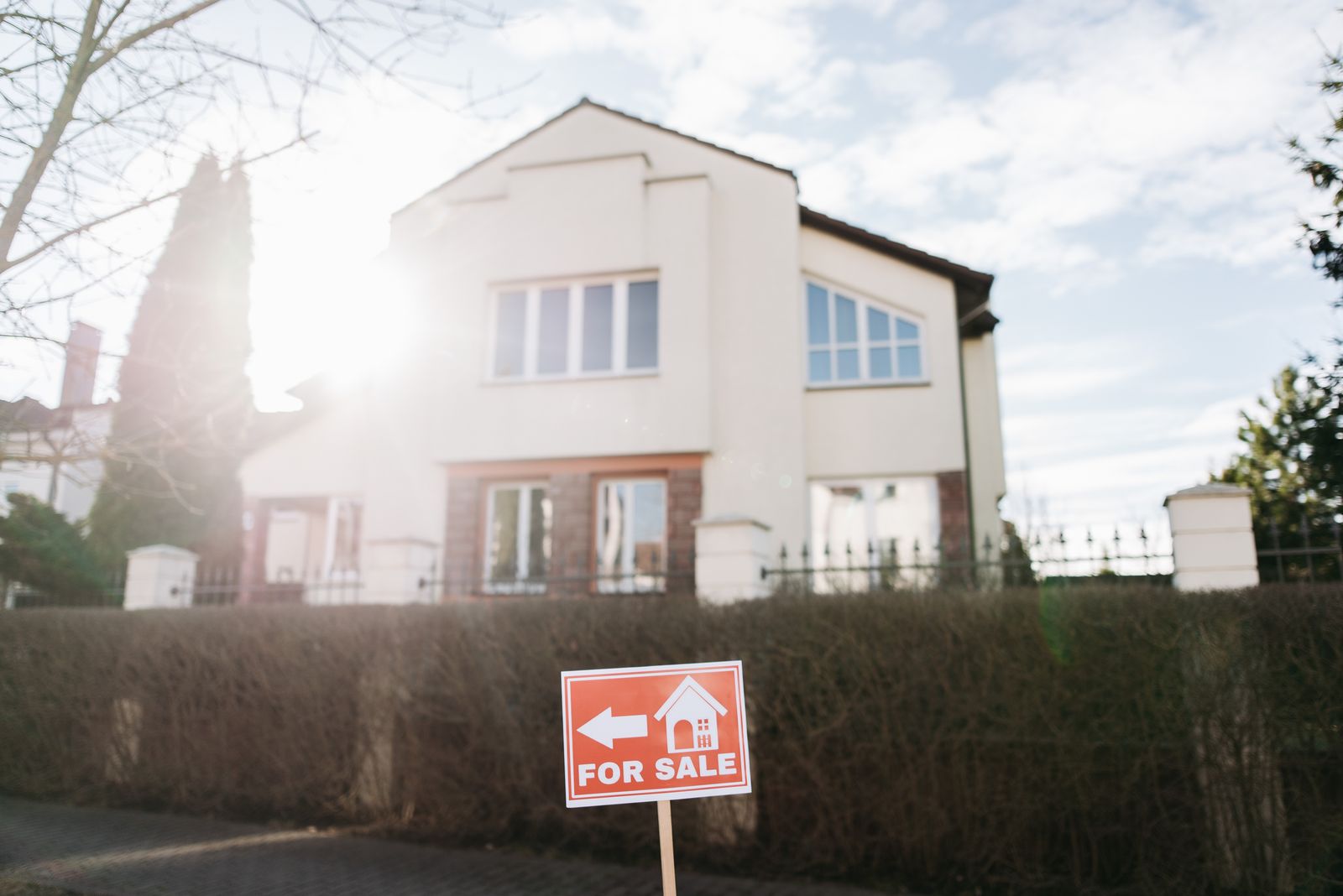 A red 'For Sale' yard sign in front of a residential home