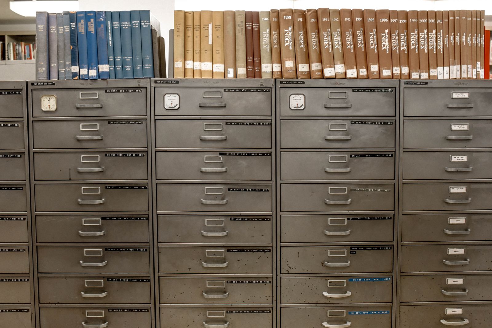 Rows of wooden archive drawers and shelved bound volumes in a records room, the kind of historical file storage a retrospective appraisal draws on