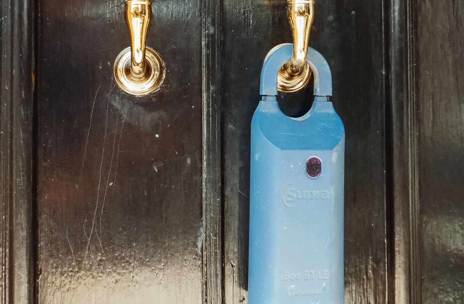 A blue combination lockbox hanging from the brass handle of a black front door