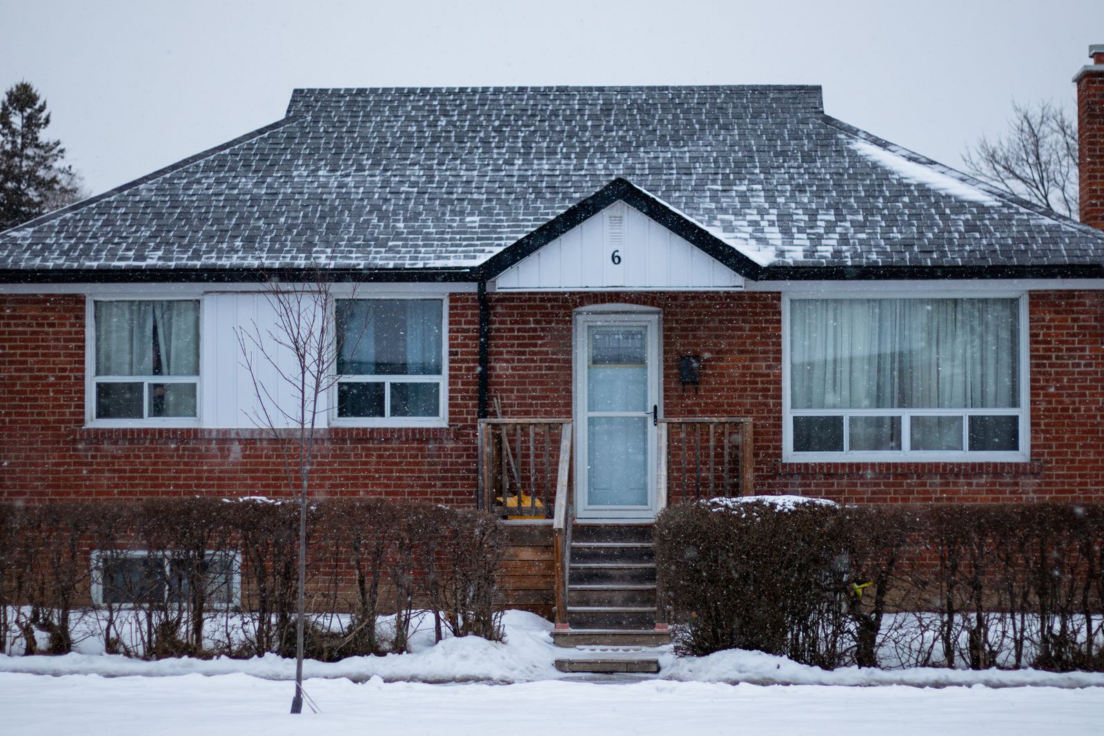 A residential brick home with snow falling and accumulated on the roof