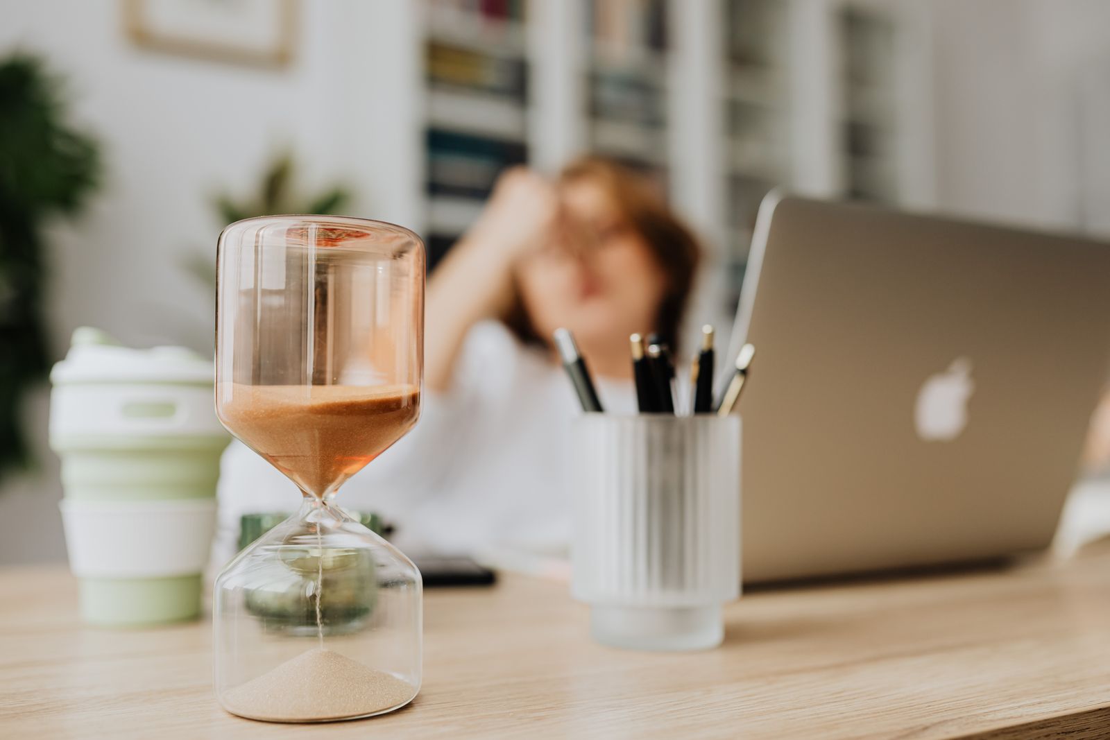 A glass hourglass with sand running through it on a light wood desk