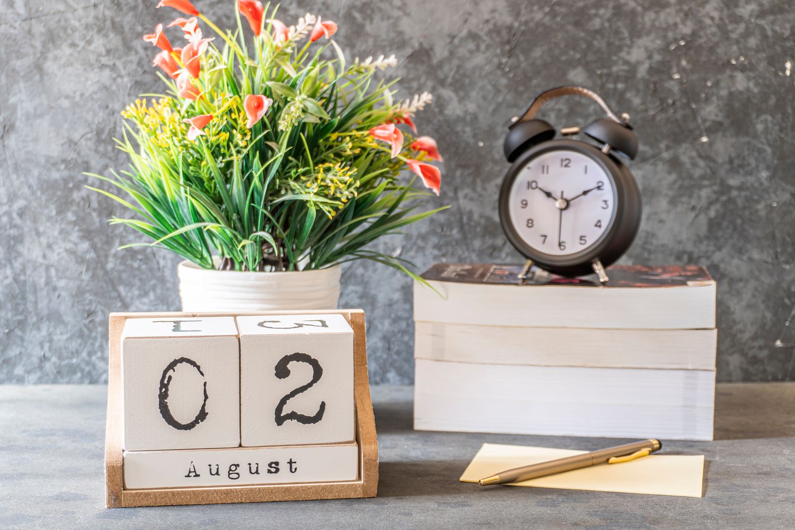 A desk arrangement with a wall calendar, an analog clock, and a stack of books