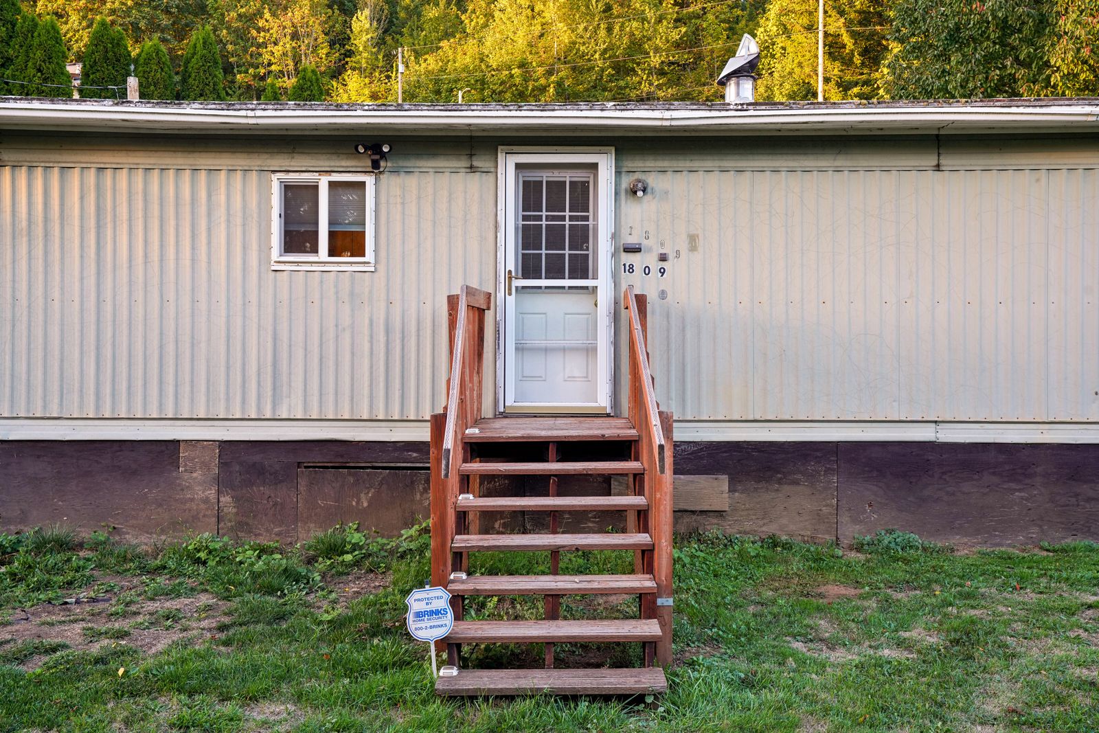Exterior of a single-section manufactured home with light siding, skirting along the base, and wooden entry steps leading to the front door