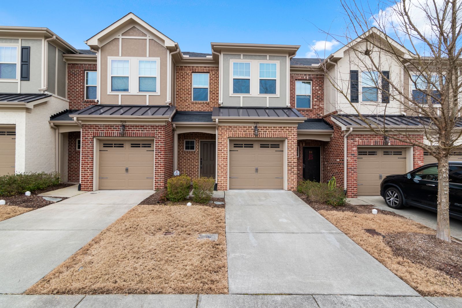 A row of attached brick townhomes with white trim, each with its own short driveway and garage, on a quiet residential street