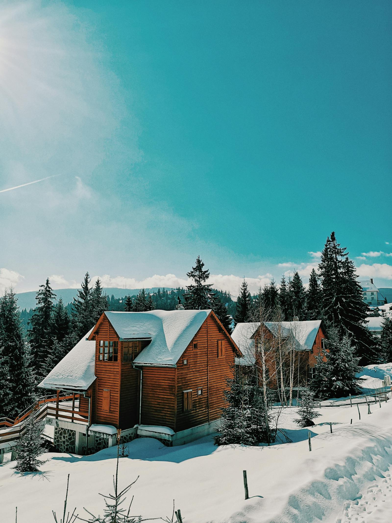 A snow-covered residential home with surrounding pines and mountains